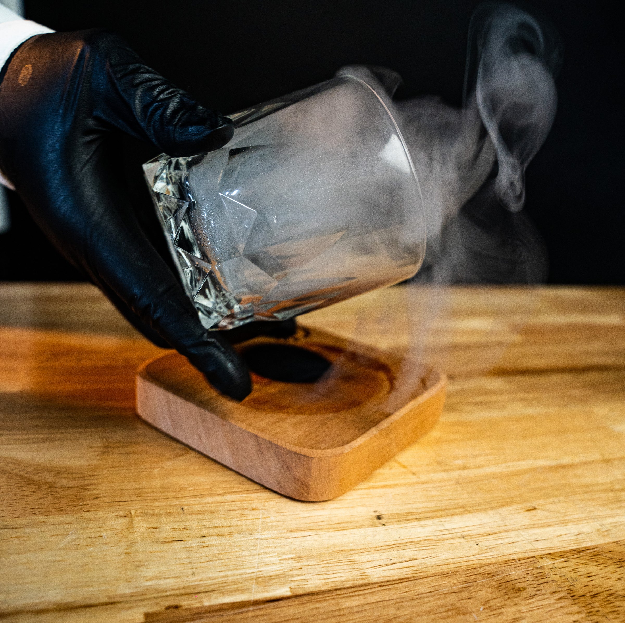 Crystal glass releasing smoke on a handcrafted reclaimed wood base from the Helius Originals luxury smoked cocktail kit.