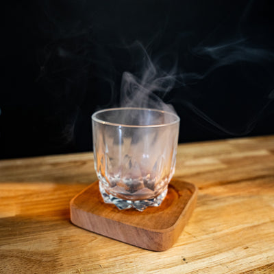 Crystal glass with smoked cocktail resting on Helius Originals Artisanal Aroma Board made from reclaimed Ontario wood.