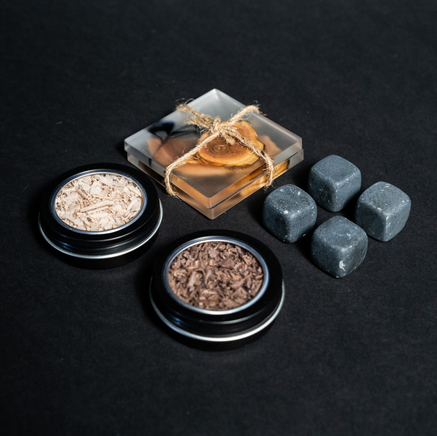 Helius Originals cocktail set accessories with whiskey stones, wood shavings tins, and a resin wood coaster tied with twine
