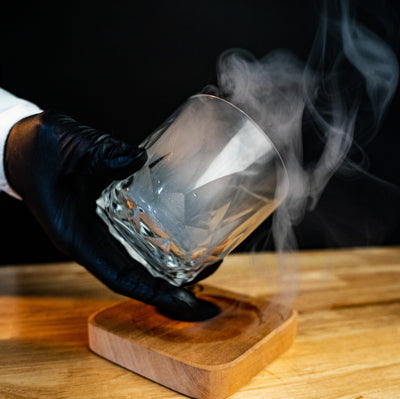 Bartender using Helius Originals Artisanal Aroma Board to smoke a cocktail glass, creating a rich aromatic presentation for mixology