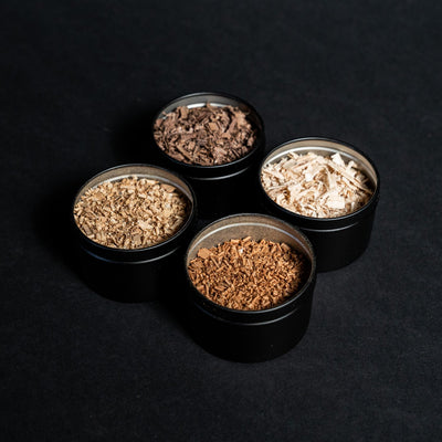 Four black tins filled with artisanal cocktail smoking wood shavings: black walnut, cherry, maple, and white oak by Helius Originals.