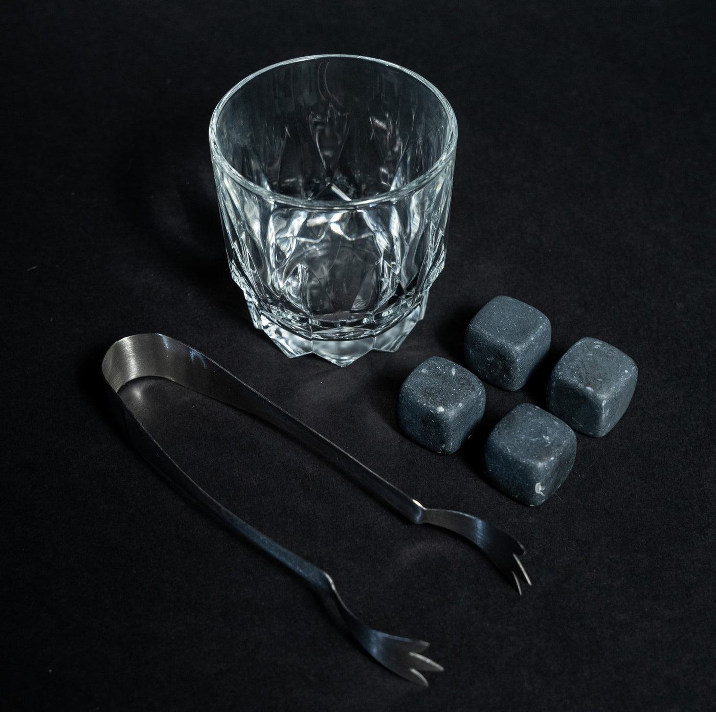 Whiskey glass with stainless steel tongs and four black whiskey stones from Helius Originals
